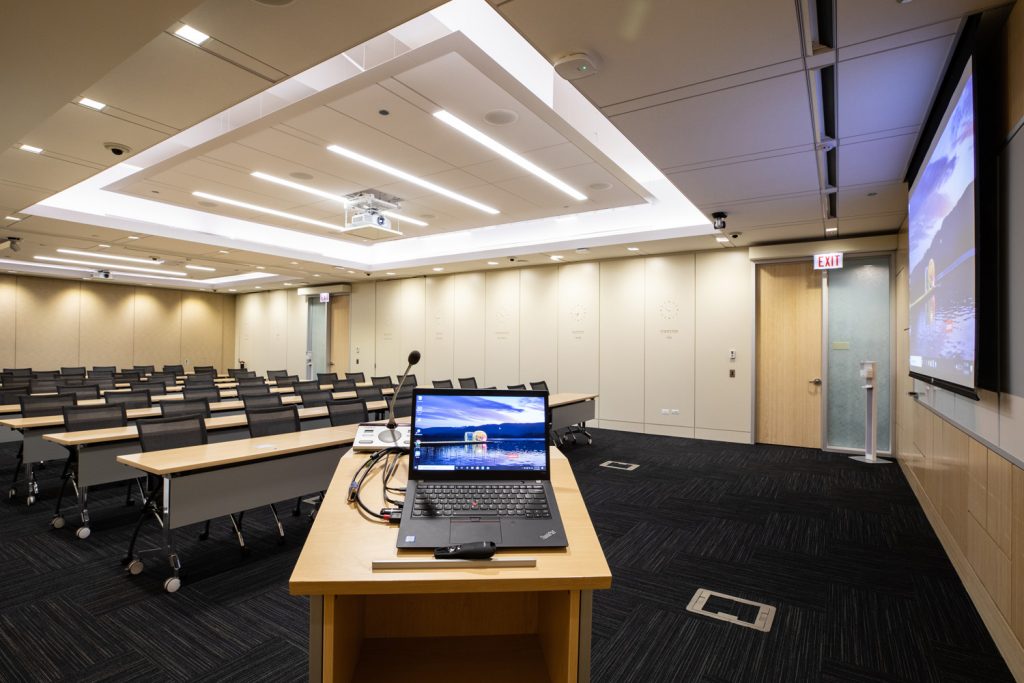 Conference Room 1AB at One Rotary Place. Photo of a large conference room with a podium & microphone,projector, and screen.
