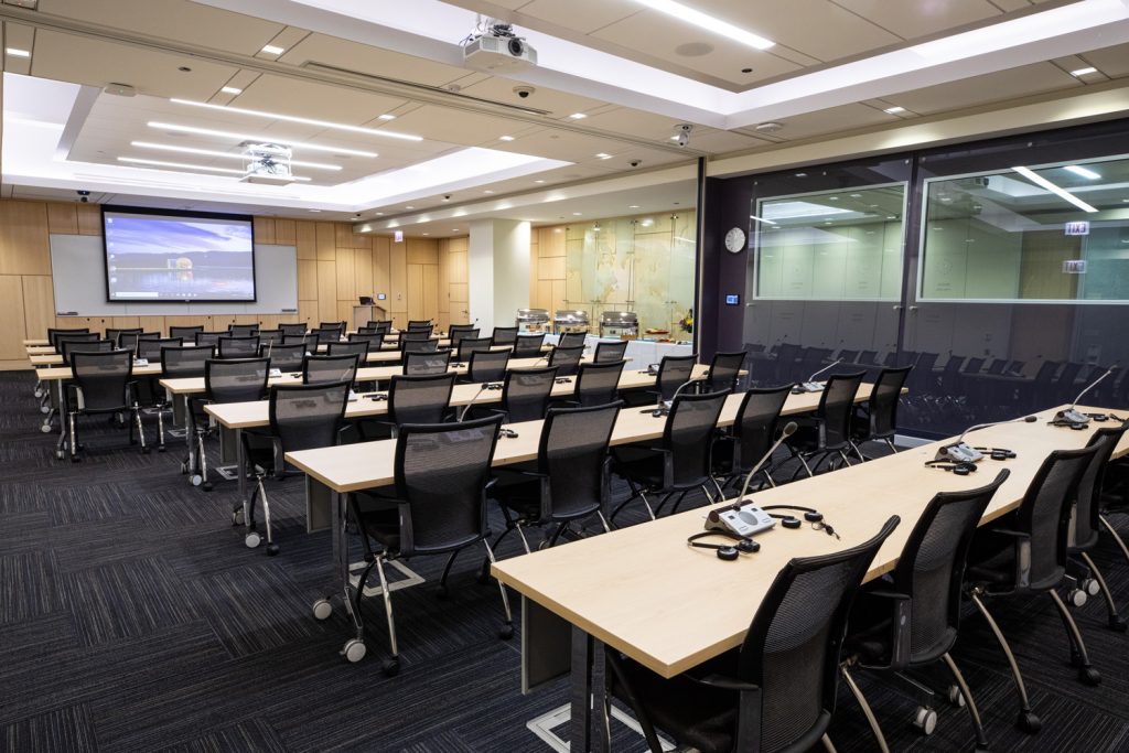 Conference Room 1A at One Rotary Place. Photo of a large conference room with a table microphones, interpretation headsets,projector and screen.