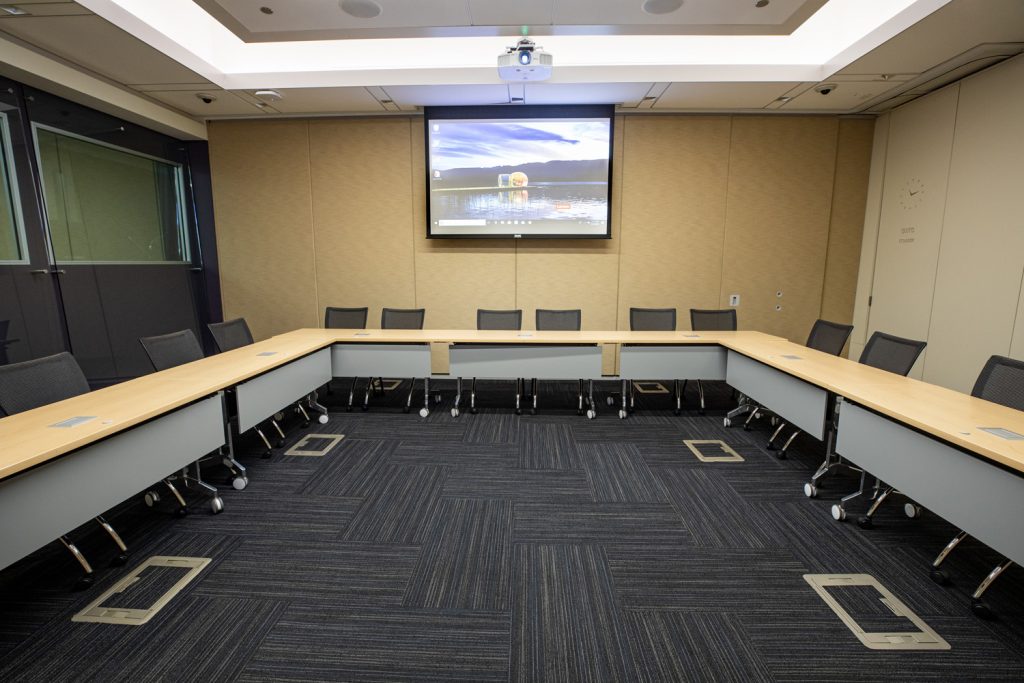 Conference Room 1B at One Rotary Place. Photo of a large conference room with tables & chairs, a projector, and screen.