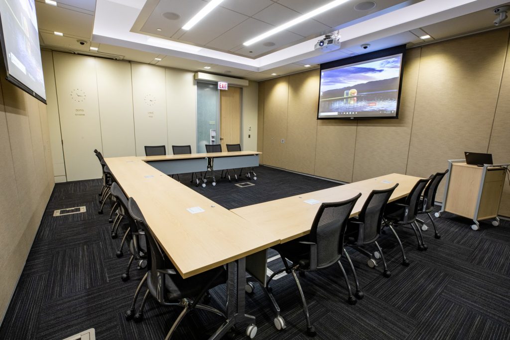 Conference Room 1B at One Rotary Place. Photo of a large conference room with a podium & laptop, a projector, and screen.