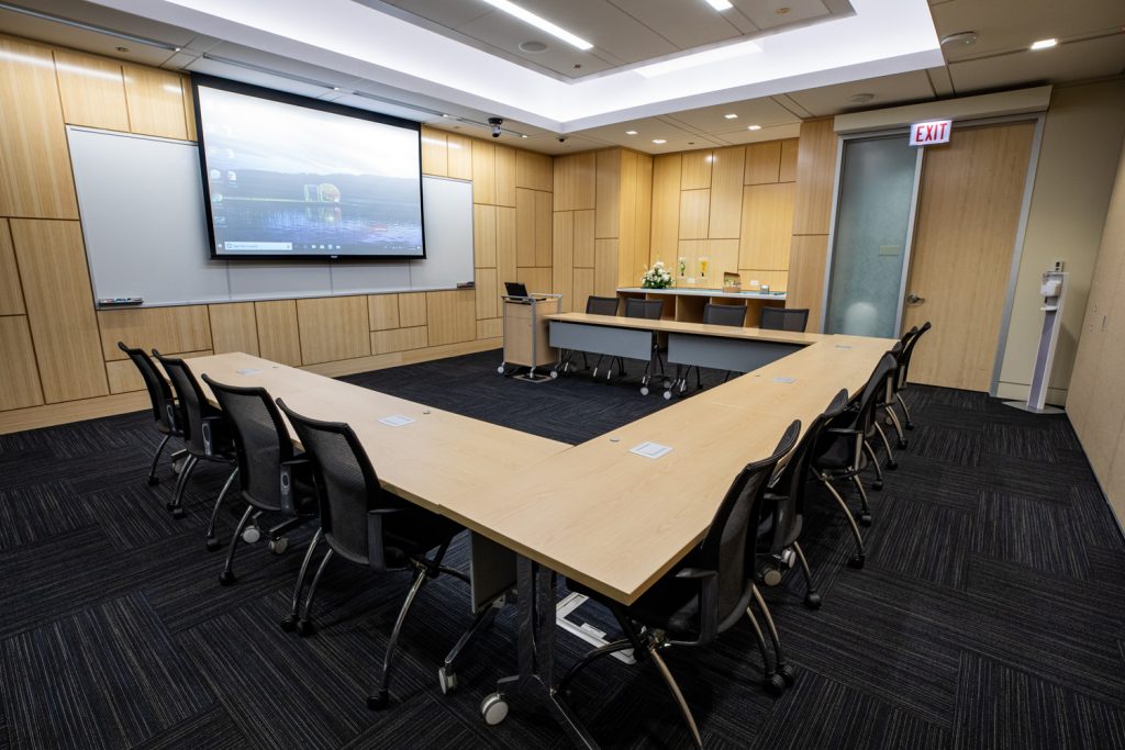 Conference Room 1C at One Rotary Place. Photo of a large conference room with tables & chairs, a projector, and screen.
